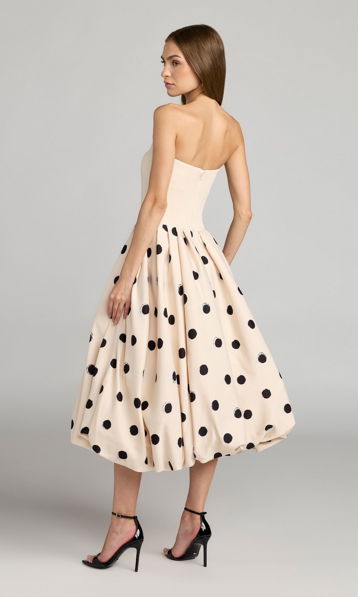 A woman models the Mac Duggal 21234 Semi-Formal Polka Dot Midi Dress, featuring a strapless bodice and fit-and-flare silhouette, paired with black high-heeled sandals against a plain background.